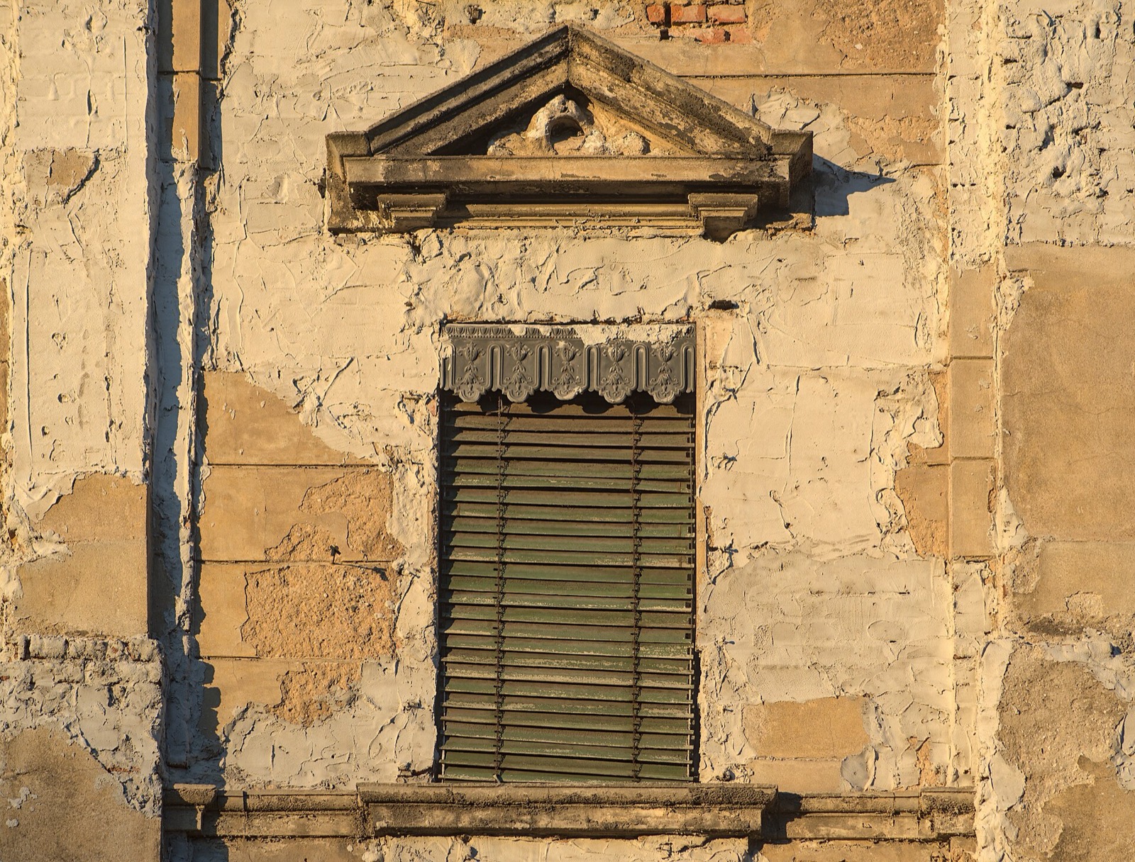 Historisches Fenster mit Holzrolladen in verwitterter Putzfassade.